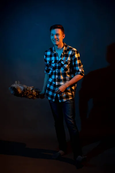 A guy in a plaid shirt with a dust brush on a dark background illuminated by blue and yellow light — Stockfoto