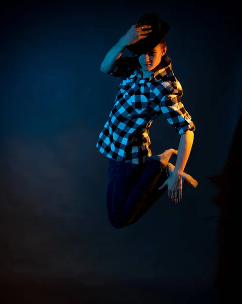 A young man in a plaid shirt jumps on a dark background illuminated by blue and yellow light — Stockfoto