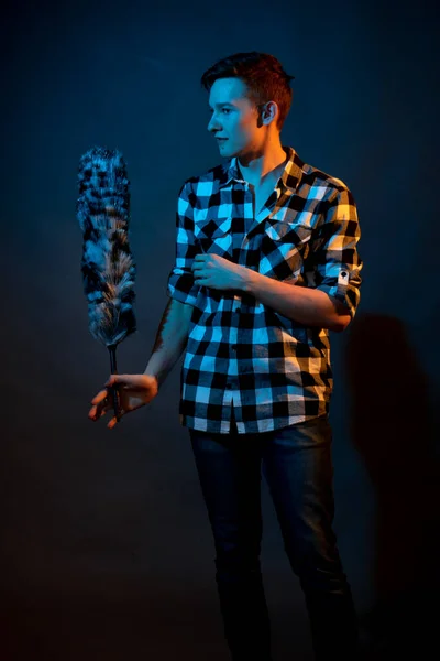 A guy in a plaid shirt with a dust brush on a dark background illuminated by blue and yellow light — 图库照片