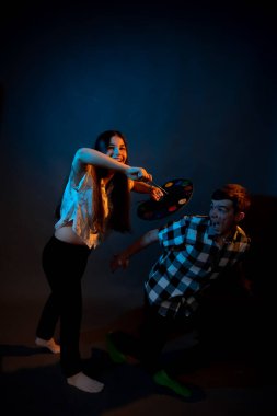 A girl paints a guy in the studio on a dark background illuminated by multicolored light
