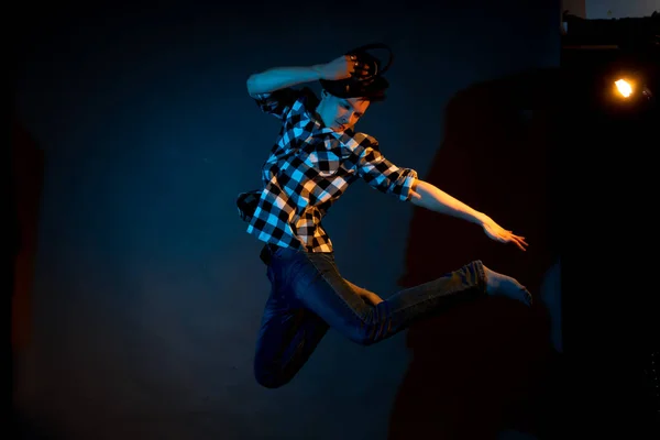 A young man in a plaid shirt jumps on a dark background illuminated by blue and yellow light — Photo