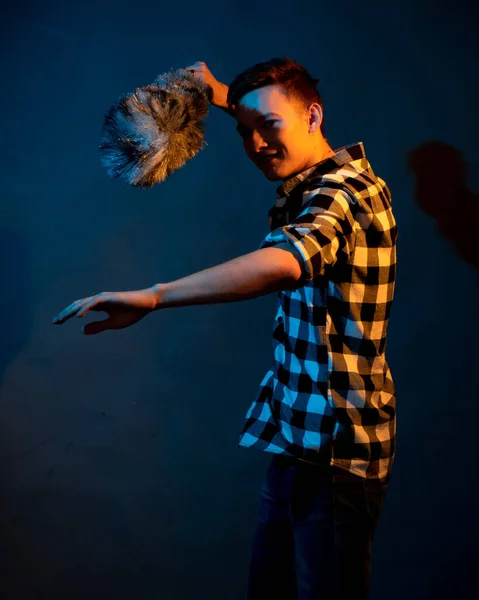 A guy in a plaid shirt with a dust brush on a dark background illuminated by blue and yellow light — Photo
