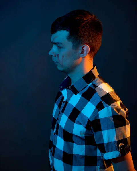 A young man in a plaid shirt jumps on a dark background illuminated by blue and yellow light — Foto de Stock