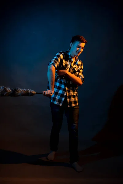 A guy in a plaid shirt with a dust brush on a dark background illuminated by blue and yellow light — Stock fotografie