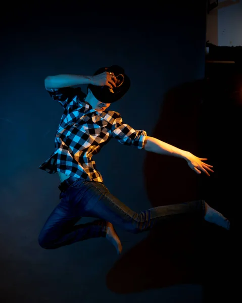 A young man in a plaid shirt jumps on a dark background illuminated by blue and yellow light — Photo