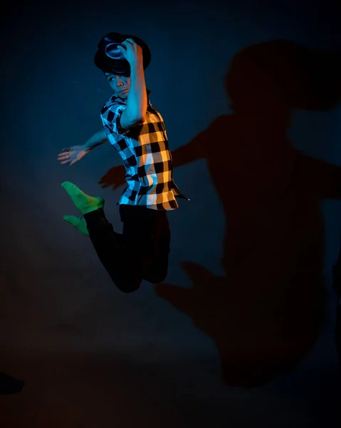 A young man in a plaid shirt jumps on a dark background illuminated by blue and yellow light — Photo