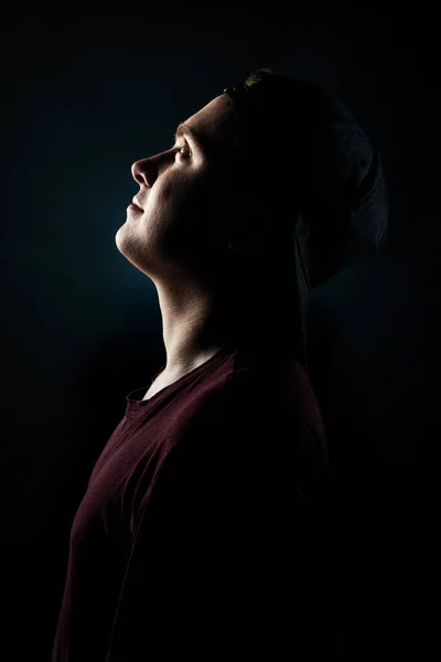 Πορτραίτο ενός νεαρού άνδρα σε ένα καπέλο κοιτάζοντας προς τα πάνω, σε προφίλ σε μαύρο φόντο — Φωτογραφία Αρχείου