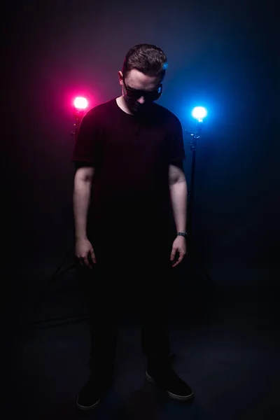 Ο τύπος στέκεται με γυαλιά ηλίου στο φόντο του καπνού, φωτίζεται από το μπλε και κόκκινο φως — Φωτογραφία Αρχείου