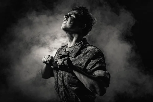 Retrato blanco negro de un joven soldado en colores de combate, cicatrices y moretones, sosteniendo un machete sobre un fondo negro con humo — Foto de Stock
