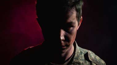 Yaralı ve savaş boyalı bir askerin portresi, kırmızı dumanın arka planında yarı aydınlık.