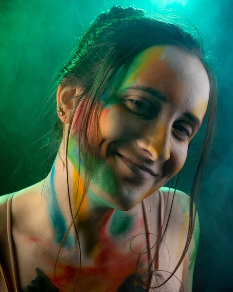 A close-up portrait of a girl with smears of paint on her face against the background of smoke illuminated by blue light — Stock Photo, Image