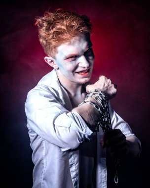 Yüzünde joker makyajı ve ellerinde zinciriyle kırmızı ışıkla aydınlatılan dumanın arka planına karşı bir manyak.