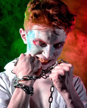 Yüzünde kan ve ellerinde zinciriyle kırmızı ve yeşil ışıkla aydınlatılan dumanın arka planına karşı saldırgan psikopat.