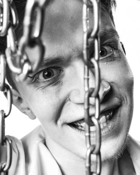 Bir manyağın siyah beyaz portresi. Yüzüne zincir dayamış ve beyaz arka planda acımasızca gülümsüyor.