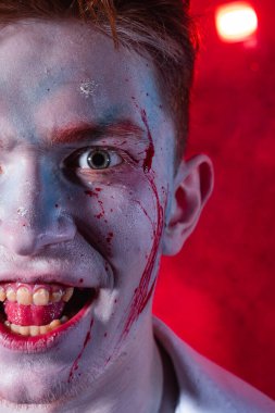 Makyajlı ve yüzünde kan olan bir psikopat kırmızı ışıkla yanan dumanın arka planında çığlık atıyor.