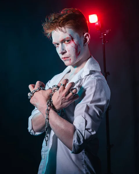Yüzünde kan ve ellerinde zincirle kırmızı ve mavi dumandan oluşan bir manyağın portresi.
