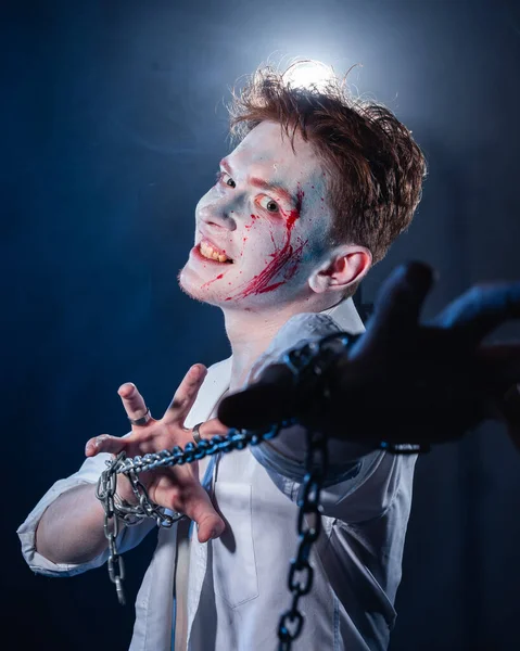 Yüzünde saldırganlıkla makyaj yapan bir psikopat kameraya mavi dumanın arka planına bakıyor.