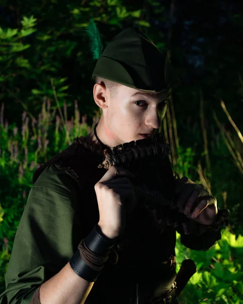 Peter Pan plays a flat sitting in the grass against the backdrop of the forest. Cosplay on Peter Foam. Robin Hood