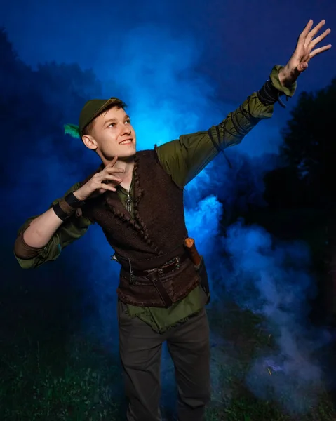 Cosplay on Peter Pan. A young man in a Peter Pan costume stands amid blue smoke at night
