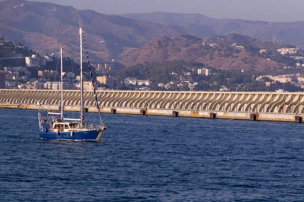 Mavi bir yelkenli Malaga 'nın limanını terk ediyor. Arka planda şehir var.