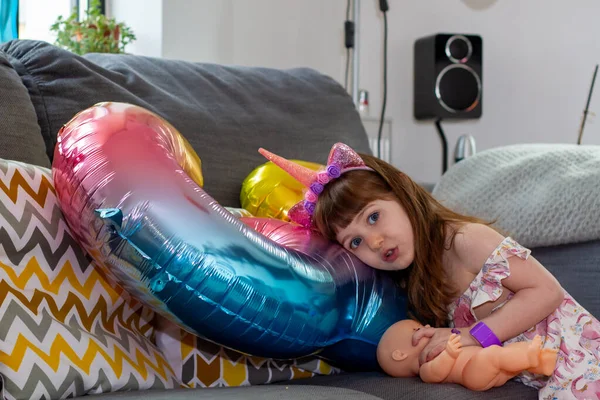 Koltukta renkli bir balon ve oyuncak bebekle oturan tatlı bir kız.