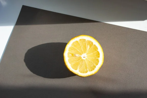 Koca bir limonun yarısı gri bir arka planda yatıyor. Gün ışığı limonla parlar