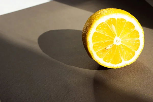 Koca bir limonun yarısı gri bir arka planda yatıyor. Gün ışığı limonla parlar