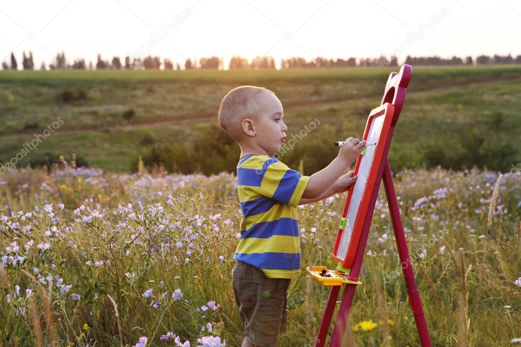 little boy paints on a canvas , landscape outdoors