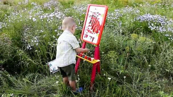 Маленький мальчик рисует на мольберте на открытом воздухе — стоковое видео