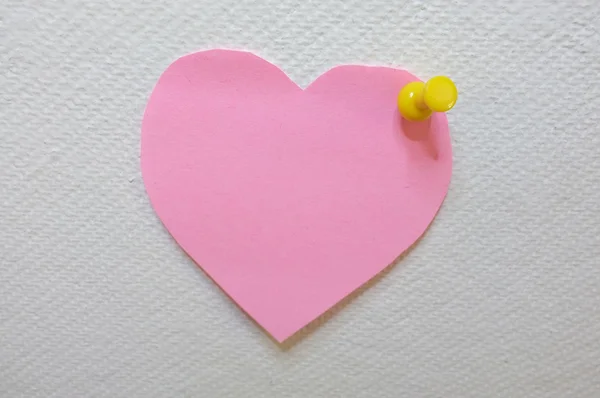 Beyaz mantar pano arka plan üzerinde yayınlanan sarı iğne ile kalp şeklinde pembe not kağıdı — Stok fotoğraf