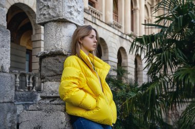  Eski bir binanın ve palmiye ağaçlarının arkasında sarı ceketli genç bir kız. Seyahat ve şehir turizmi.