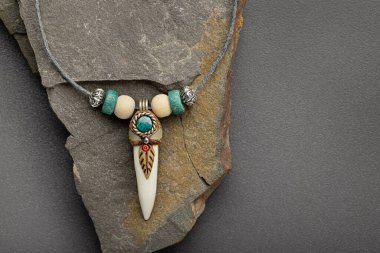 Gümüş kolye, timsah dişi ve turkuaz kaplı taş bir tabakta. Gri arkaplan, yakın plan, stüdyo çekimi.