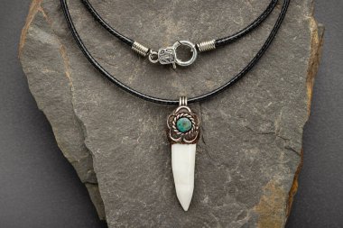 Ağda ipiyle tılsım. Gümüş kaplı bir timsah dişi taştan bir tabağın arka planında.