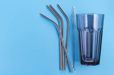 Temizlik fırçalı tekrar kullanılabilir metal pipetler, mavi arka planda büyük mavi kokteyl bardakları. Boşluğu kopyala, stüdyo çekimi.