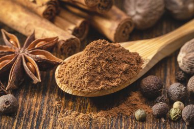 Kahverengi bir masada bir çift baharat. Tarçınlı ve tarçınlı tahta kaşık. Anason, tüm hindistan cevizleri, tüm bezelyeler.