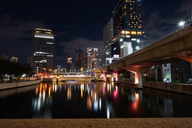 Osaka, Japonya - 26 Ekim 2025 - Dojima Nehri üzerindeki Suishaboshi Köprüsü 'nden Kita-ku' daki aydınlık ofis kuleleriyle gece görüşü; Nakanoshima Adası ve Tosabori Nehri solda yer almaktadır.