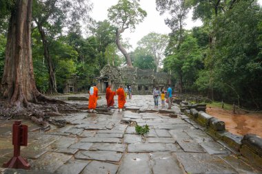 Angkor, Kamboçya - 7 Kasım 2025 - Turuncu dini cüppeli Budist keşişler ve Angkor UNESCO Dünya Mirası Alanındaki 12. yüzyıldan kalma bir manastır Prasat Ta Prohm 'u ziyaret edenler yağmurlu bir tropikal günde