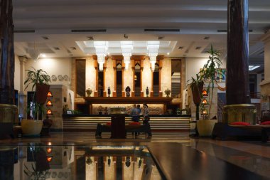 Siem Reap, Kamboçya - 5 Kasım 2025 - Angkor Miracle Resort and Spa 'nın ana lobisi, 5 yıldızlı lüks bir otel, koyu ahşap sütunlar, Khmer tarzı heykeller ve süslemeler ve arka aydınlatma tezgahı