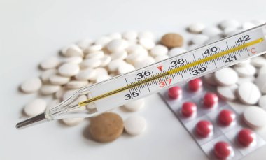 Cıva termometresi hapların arka planında vücut ısısının 37.4 olduğunu gösteriyor.