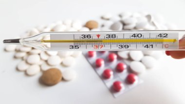 Cıva termometresi hapların arka planında vücut ısısının 37.4 olduğunu gösteriyor.