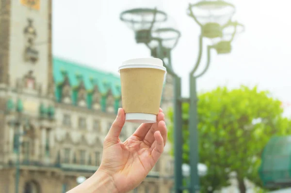 Hand holding a takeaway coffee cup in a city.