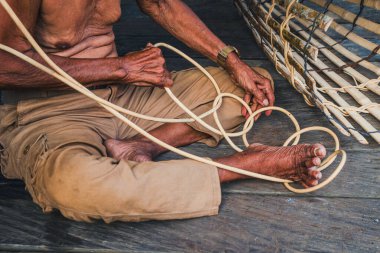 Geleneksel bir sepet tuzağı yapmak için bambu şeritleri dokumakta olan bir Dayak Benuaq 'ın yakın plan çekimi, yerel zanaatkarlık, kültür mirası ve Borneo kırsalında ustalıkla yapılmış el işi..