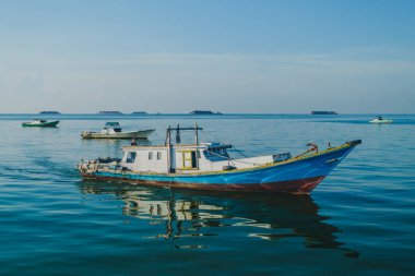 Balikpapan, Endonezya - 8 Kasım 2025. Orta büyüklükte, parlak bir Endonezya balıkçı teknesi beyaz kabini ve mavi gövdesi ile sakin, yansıtıcı mavi denizde yol alır..