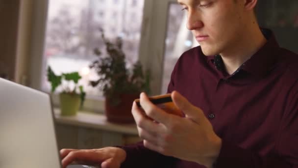 Молодий чоловік використовує комп'ютер для онлайн-покупки з кредитною карткою. повільний рух — стокове відео