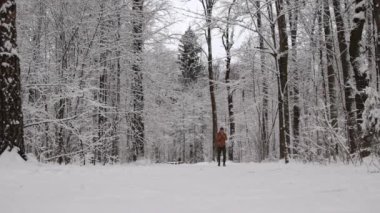 Karla kaplı bir ormanda ağır çekimde yürüyen bir adam.