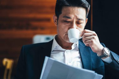 Kahve içip gazete okuyan ciddi bir iş adamı.
