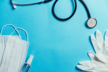 Cerrahi maske, antiseptik dezenfektan spreyi, eldiven ve steteskop mavi arka planda fotokopi alanı. Covid-19 virüs koruma kavramı
