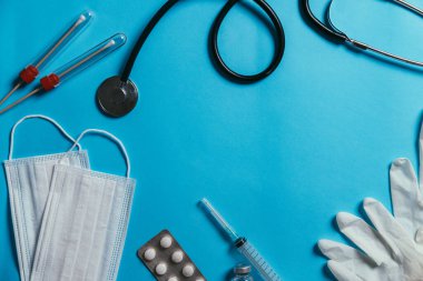 Mavi arka planda tıbbi malzemeler. Haplı maske, steteskop, aşı, şırınga, şırınga, mavi arka planda izole edilmiş tıbbi malzeme, üst görünüm, düz yüz, yukarıdan çekim, Covid-19 virüs koruma konsepti