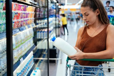 Süpermarketten süt alan bir kadın. Genç bir kadın markette sütün etiketini kontrol ediyor. Perakende satış ve tüketim kavramı