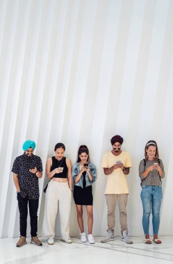 Mutlu bir grup çok kültürlü arkadaş beyaz duvarlara karşı akıllı telefonlar kullanıyor gülümseyen ve cep telefonlarıyla eğlenen yaşlı insanlara karşı. Teknoloji bağımlılığı kavramı